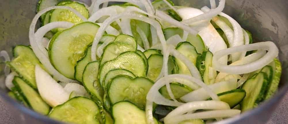 A bowl of cucumbers and onions in a metal bowl.