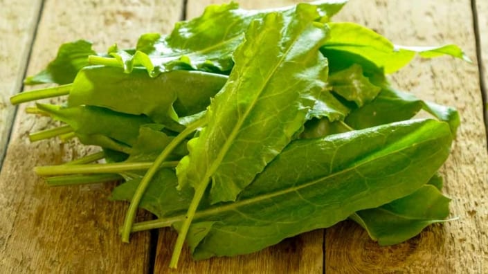 A pile of green leafy vegetables on top of a wooden table.