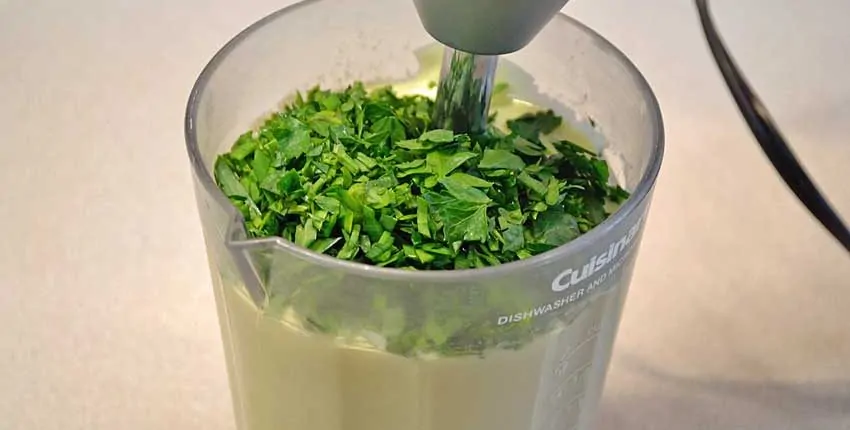 A blender filled with green liquid and some parsley.