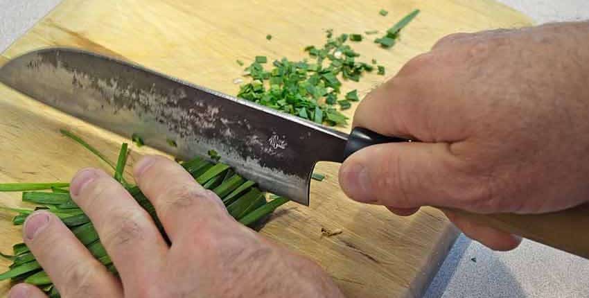 A person is cutting some green vegetables with a knife.