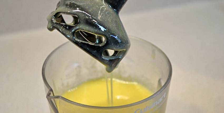 A glass of orange juice being stirred with a metal mixer.