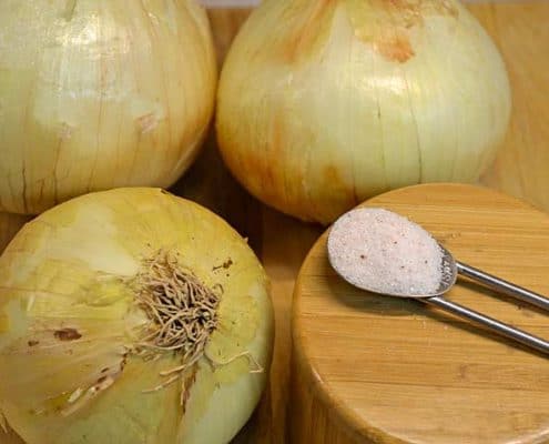 Onions are sitting on a wooden board next to a spoon.