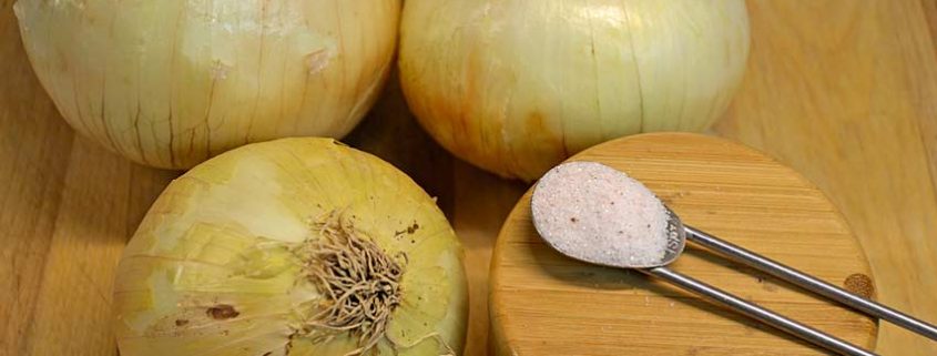 Onions are sitting on a wooden board next to a spoon.