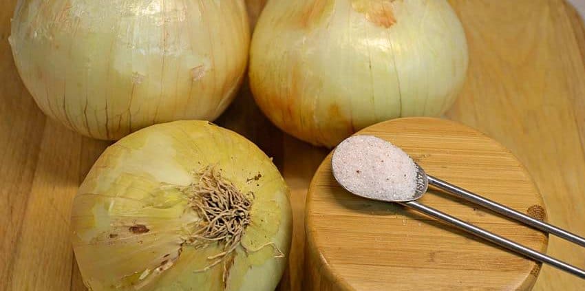 Onions are sitting on a wooden board next to a spoon.