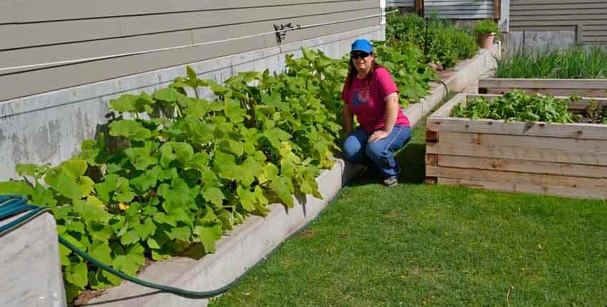 A woman kneeling down next to a garden hose.