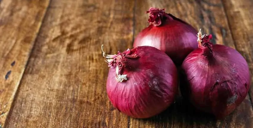Three red onions sitting on a wooden table.