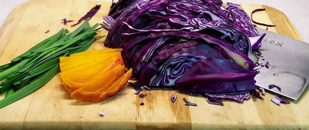 A cutting board with some purple cabbage and an orange.