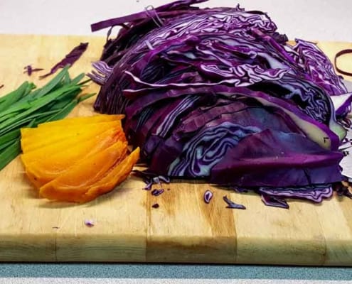 A cutting board with some purple cabbage and an orange.