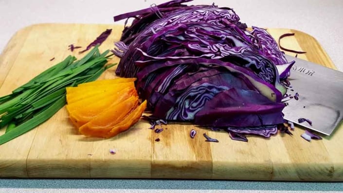 A cutting board with some purple cabbage and an orange.