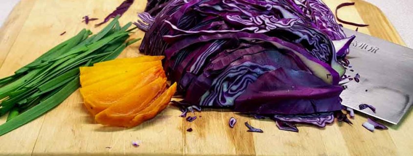 A cutting board with some purple cabbage and an orange.