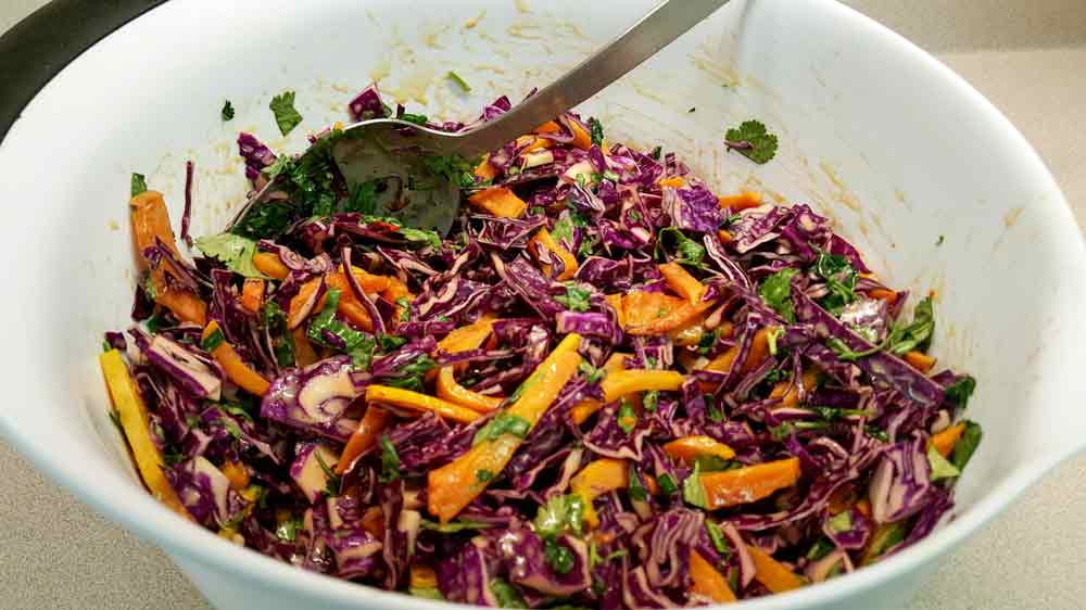 A bowl of salad with cabbage, carrots and greens.