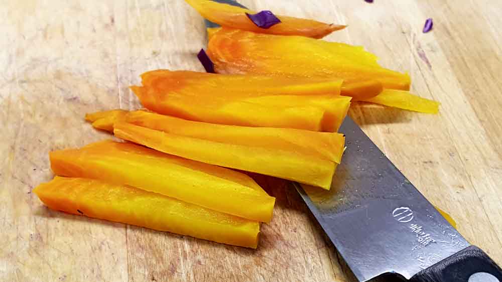 A knife and some yellow food on top of a cutting board.