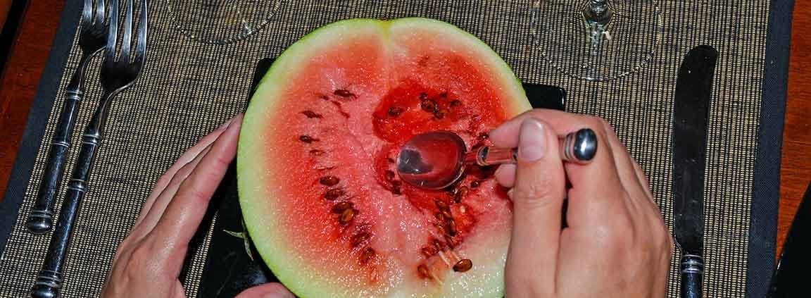 A person cutting into a watermelon with scissors.