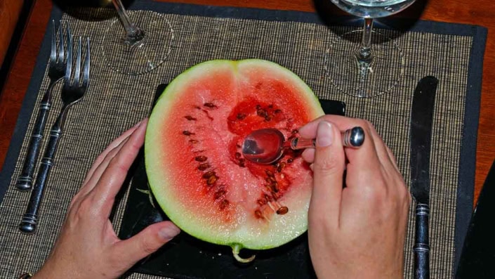 A person cutting into a watermelon with scissors.