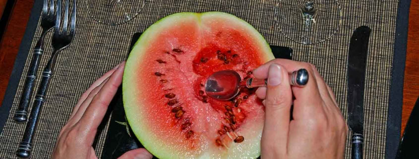 A person cutting into a watermelon with scissors.