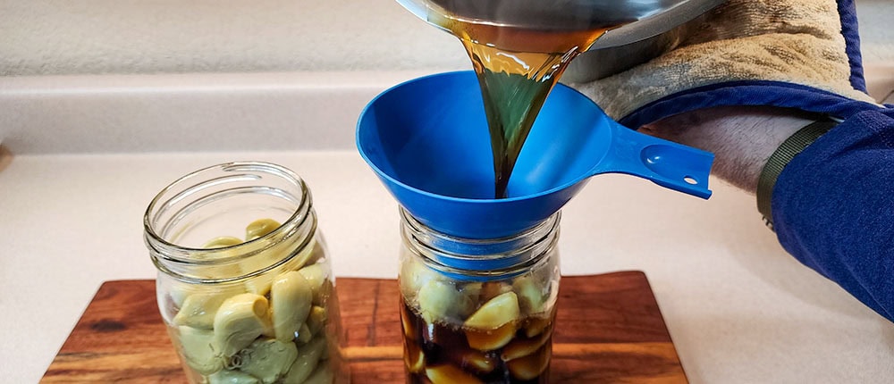 Adding hot soy brine for Korean pickled garlic.